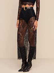 Woman wearing a sheer black Raymonde Lace Maxi Skirt with high-waisted black briefs underneath, a black lace long-sleeve crop top, and black pointed-toe, lace-up high heel boots—perfect for a stylish night out. A black belt with a gold buckle completes the look.