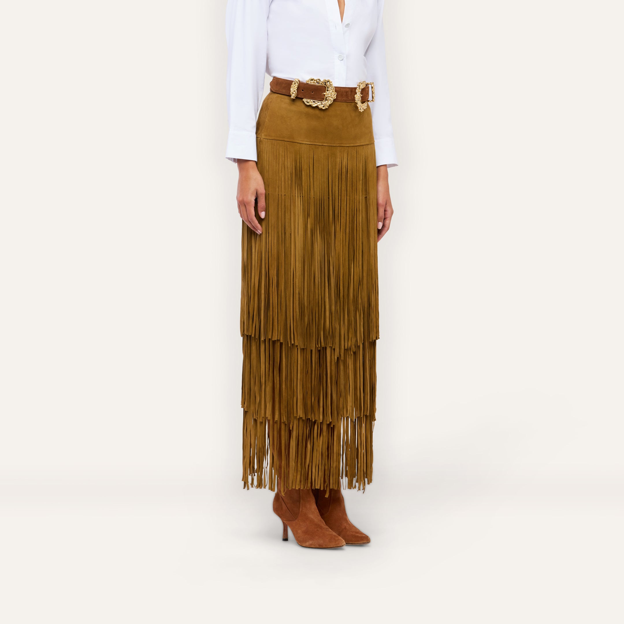 The Karoline Suede Fringe Skirt is a brown suede tiered midi skirt styled as a statement piece with a wide, ornate gold-buckled belt.