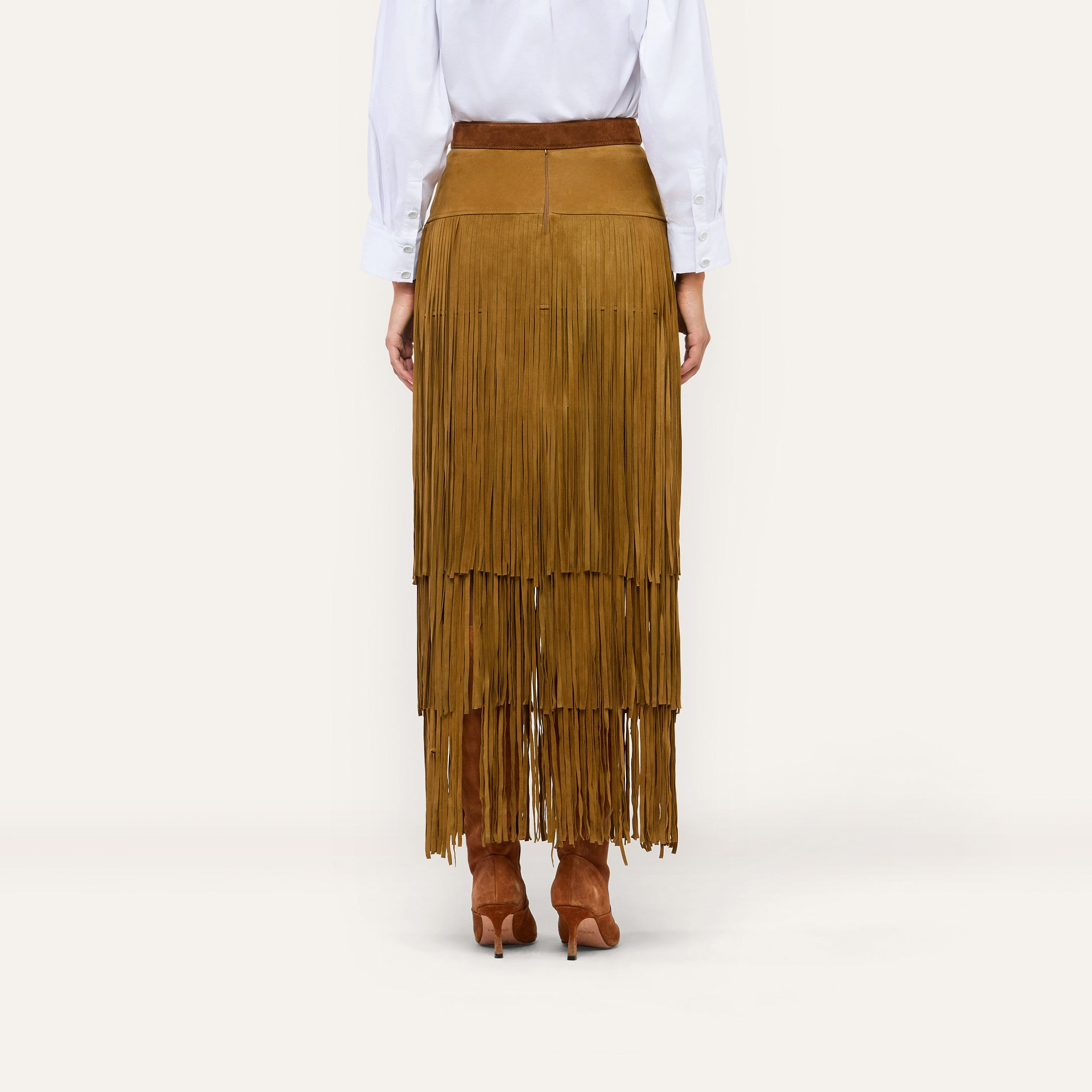 A person wears a white button-down shirt tucked into a Karoline Suede Fringe Skirt paired with brown suede heeled boots.