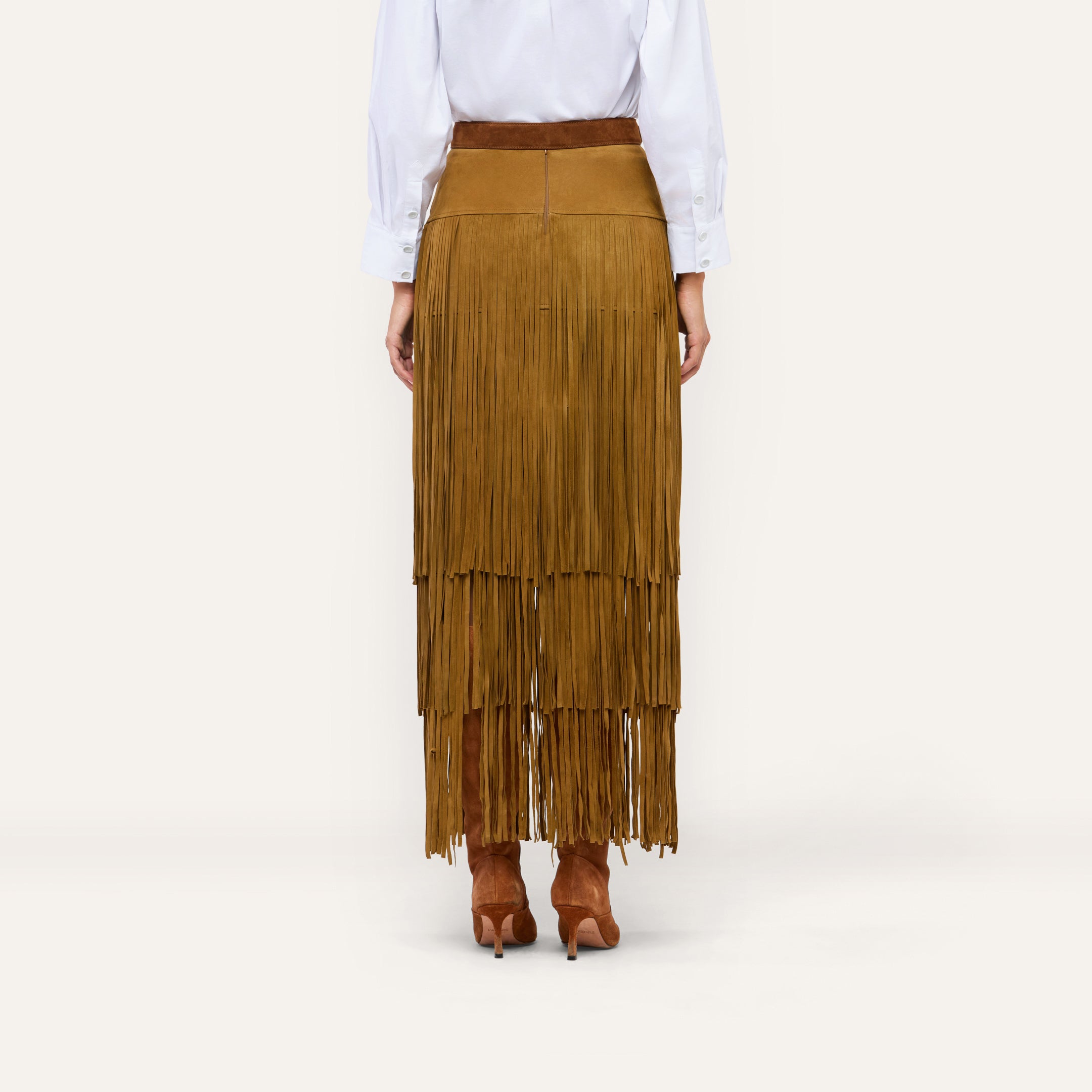 A person wears a white button-down shirt tucked into a Karoline Suede Fringe Skirt paired with brown suede heeled boots.