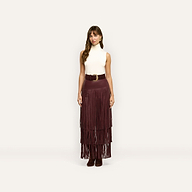 A woman wearing a sleeveless white turtleneck and a long, tiered burgundy Karoline Fringe Skirt cinched with a wide belt.