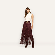 A person wears a sleeveless white turtleneck and a deep red vegan leather Karoline Fringe Skirt with a high-waisted fit and long fringe detail.