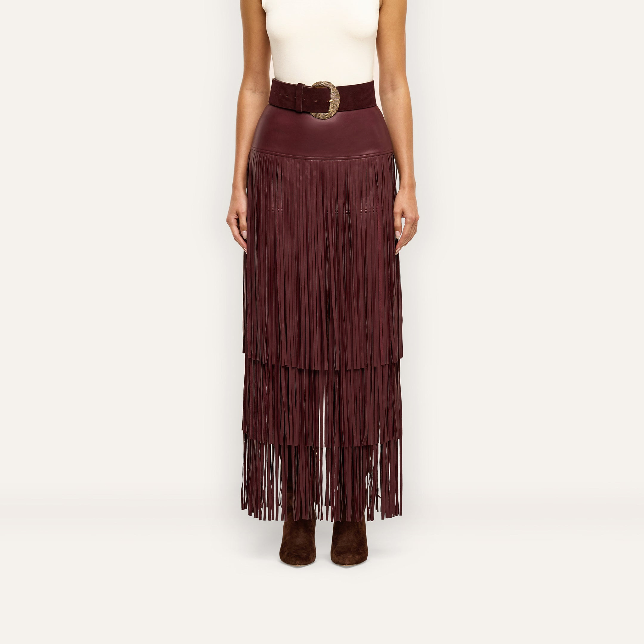 A person wearing a Karoline Fringe Skirt in deep burgundy, featuring a high-waisted, tiered midi design with a wide matching belt and gold buckle.