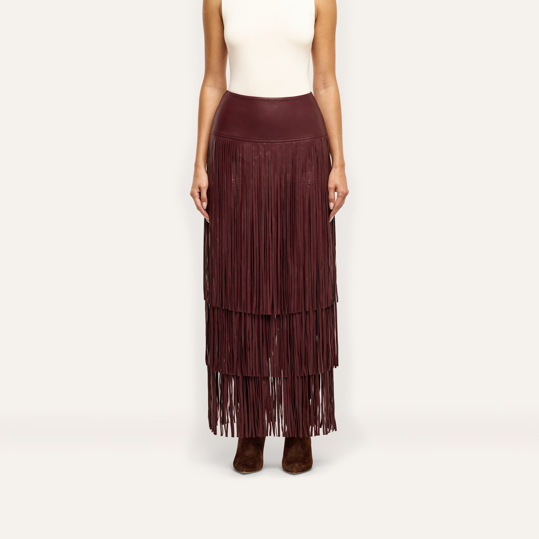 The Karoline Fringe Skirt is a floor-length, deep red tiered fringe skirt worn with a white sleeveless top and dark boots.