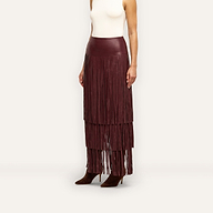 A Karoline Fringe Skirt in high-waisted, deep red vegan leather worn with a white sleeveless top and brown pointed-toe heels.