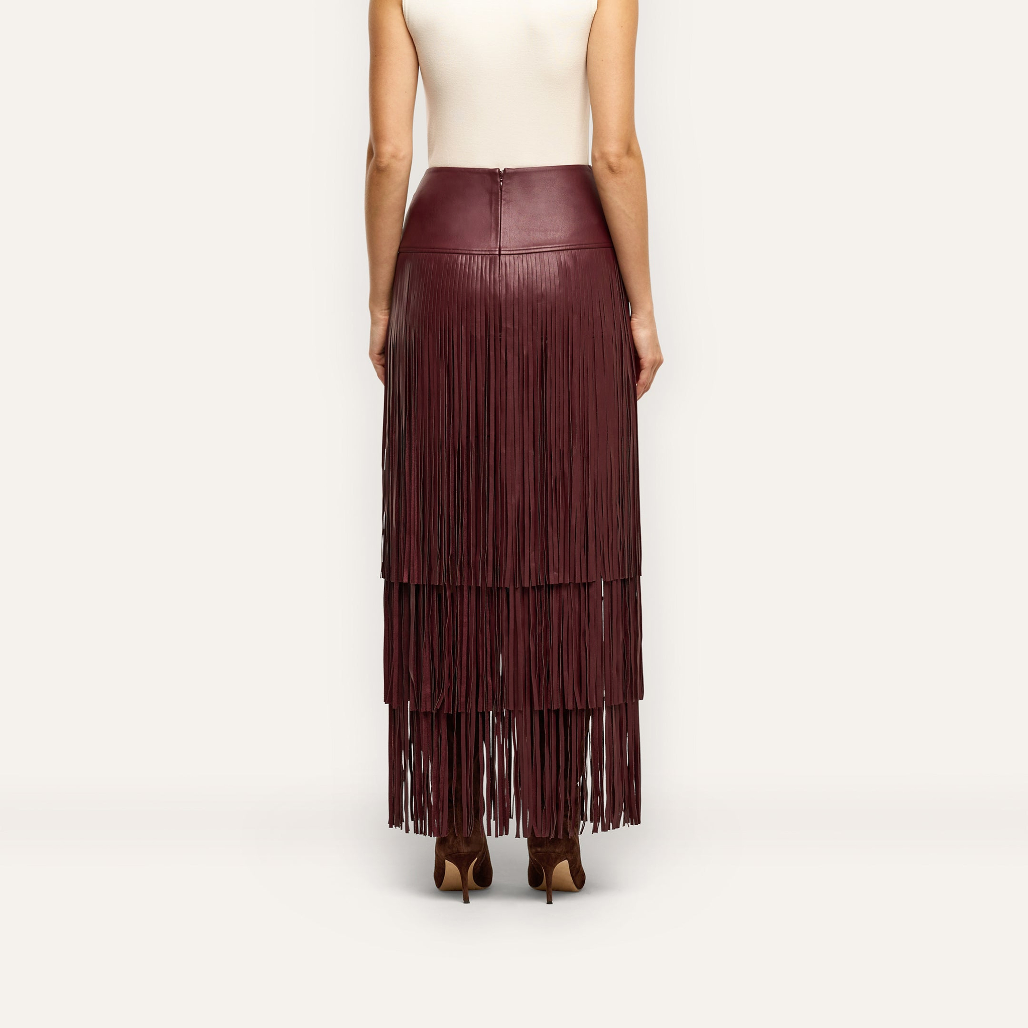 A person wearing a floor-length, deep red vegan leather Karoline Fringe Skirt featuring three tiers of fringe.