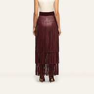 Back view of a person wearing a high-waisted burgundy Karoline Fringe Skirt in vegan leather with tiered fringe detailing that reaches the ankles.