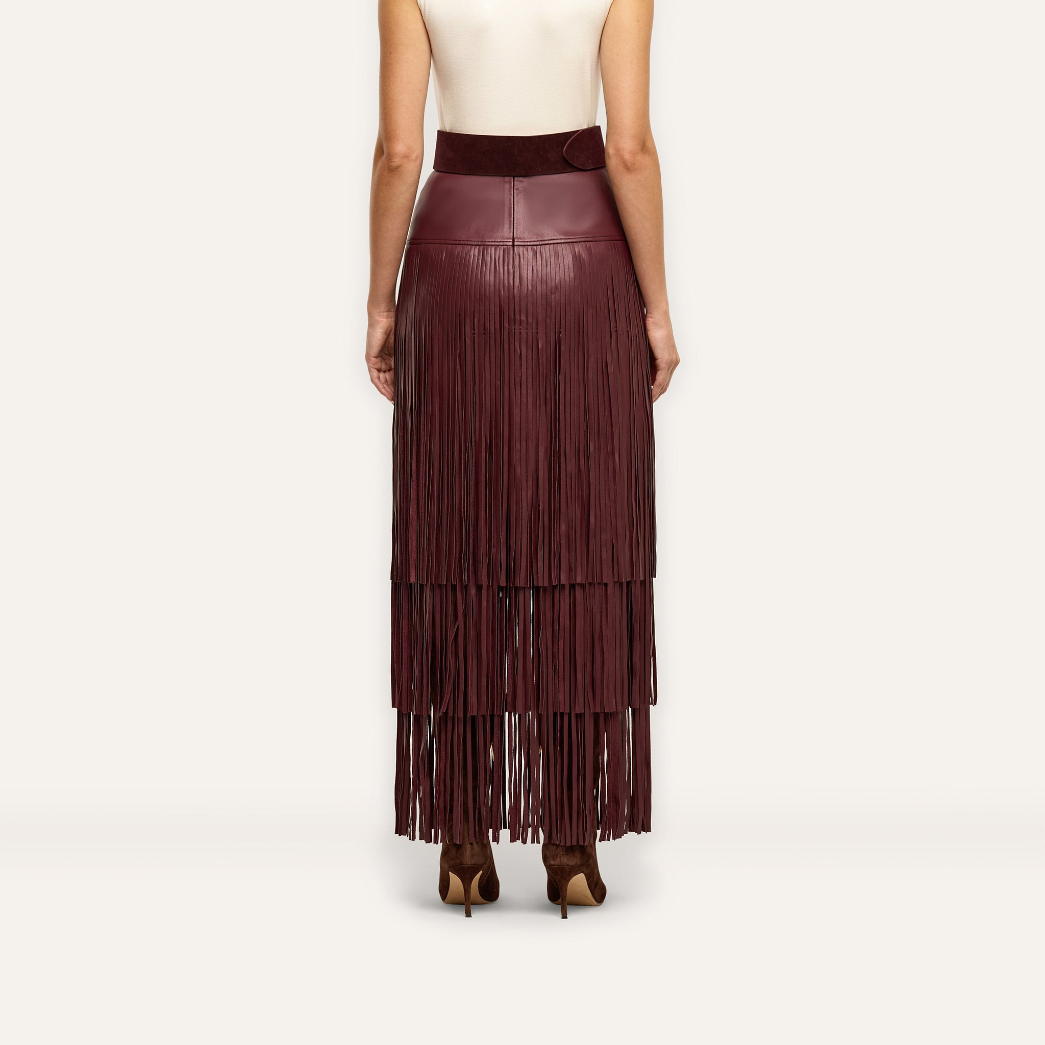 Back view of a person wearing a high-waisted burgundy Karoline Fringe Skirt in vegan leather with tiered fringe detailing that reaches the ankles.