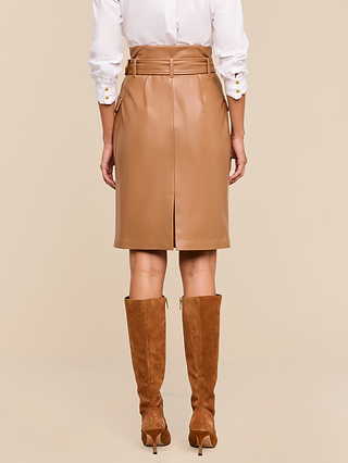 A person wearing a white shirt, the Kaelis Vegan Leather Skirt in cognac with a belt, and brown suede knee-high heeled boots is shown from the back against a neutral background.
