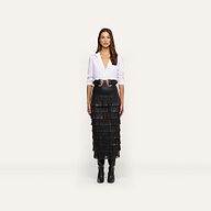 A person wearing a white button-down shirt, a double-buckle belt, and a Sevigne Fringe Skirt in a tiered black midi length.