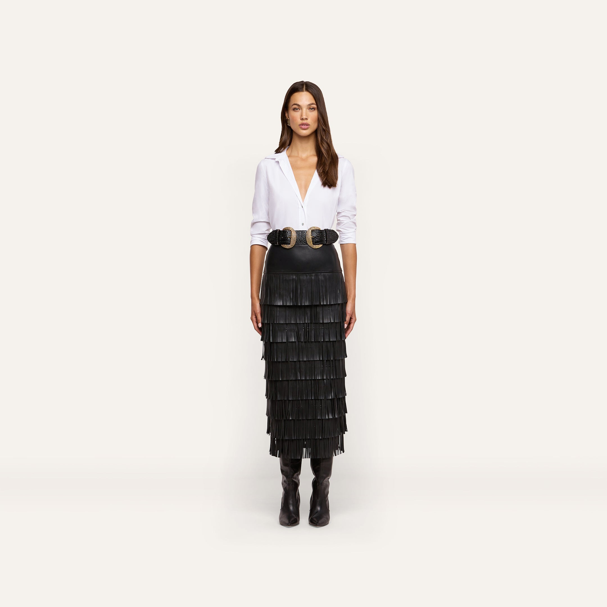 A person wearing a white button-down shirt, a double-buckle belt, and a Sevigne Fringe Skirt in a tiered black midi length.