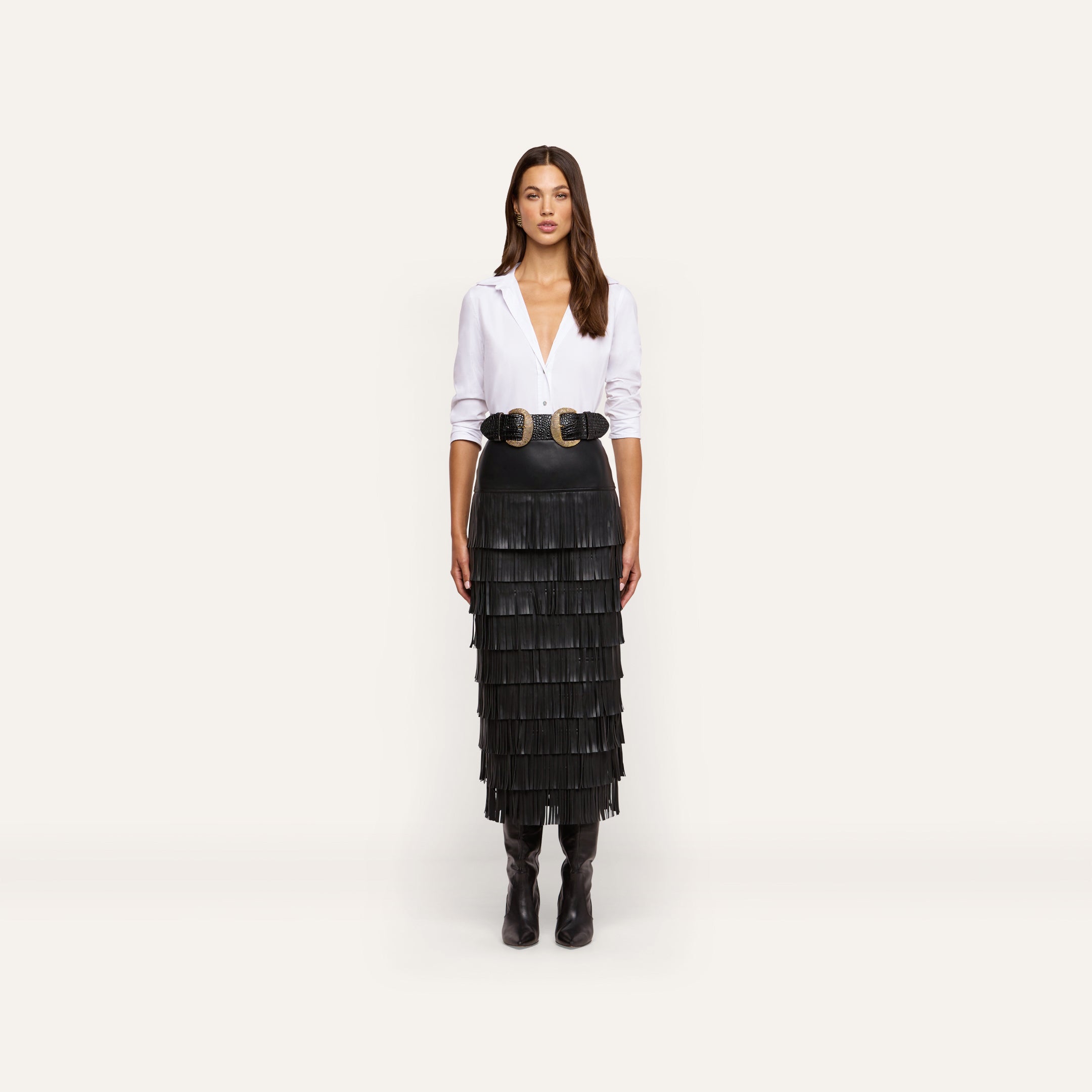 A person wearing a white button-down shirt, a double-buckle belt, and a Sevigne Fringe Skirt in a tiered black midi length.
