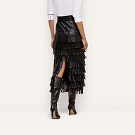A person wearing a high-waisted black Sevigne Fringe Skirt with tiered fringe, a white button-down shirt, and black high-heeled boots.