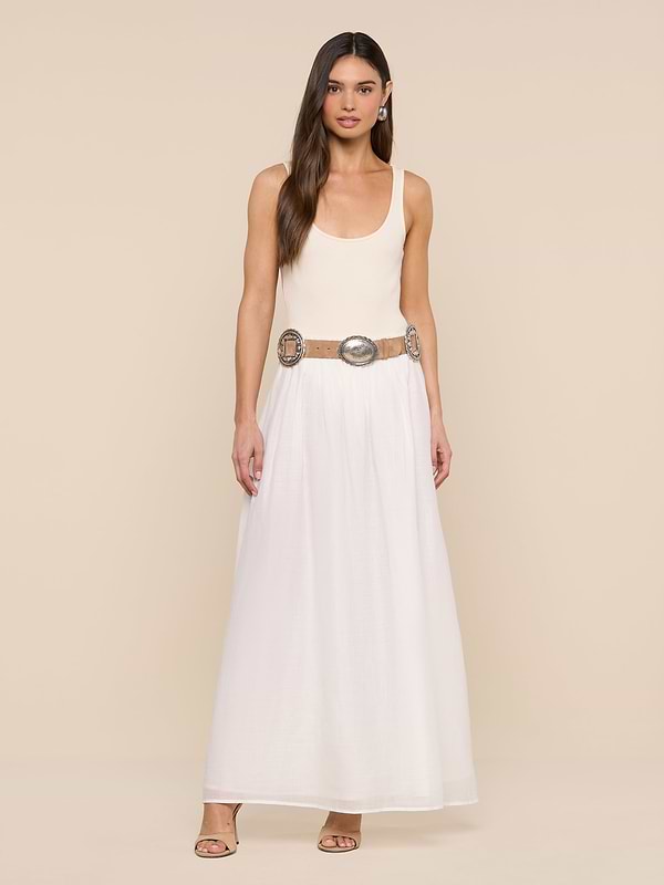 A woman stands against a white background wearing a sleeveless beige top, the Evangelina Maxi Skirt—a long, breathable white summer skirt—a wide decorative belt with large round details, hoop earrings, and open-toe shoes.