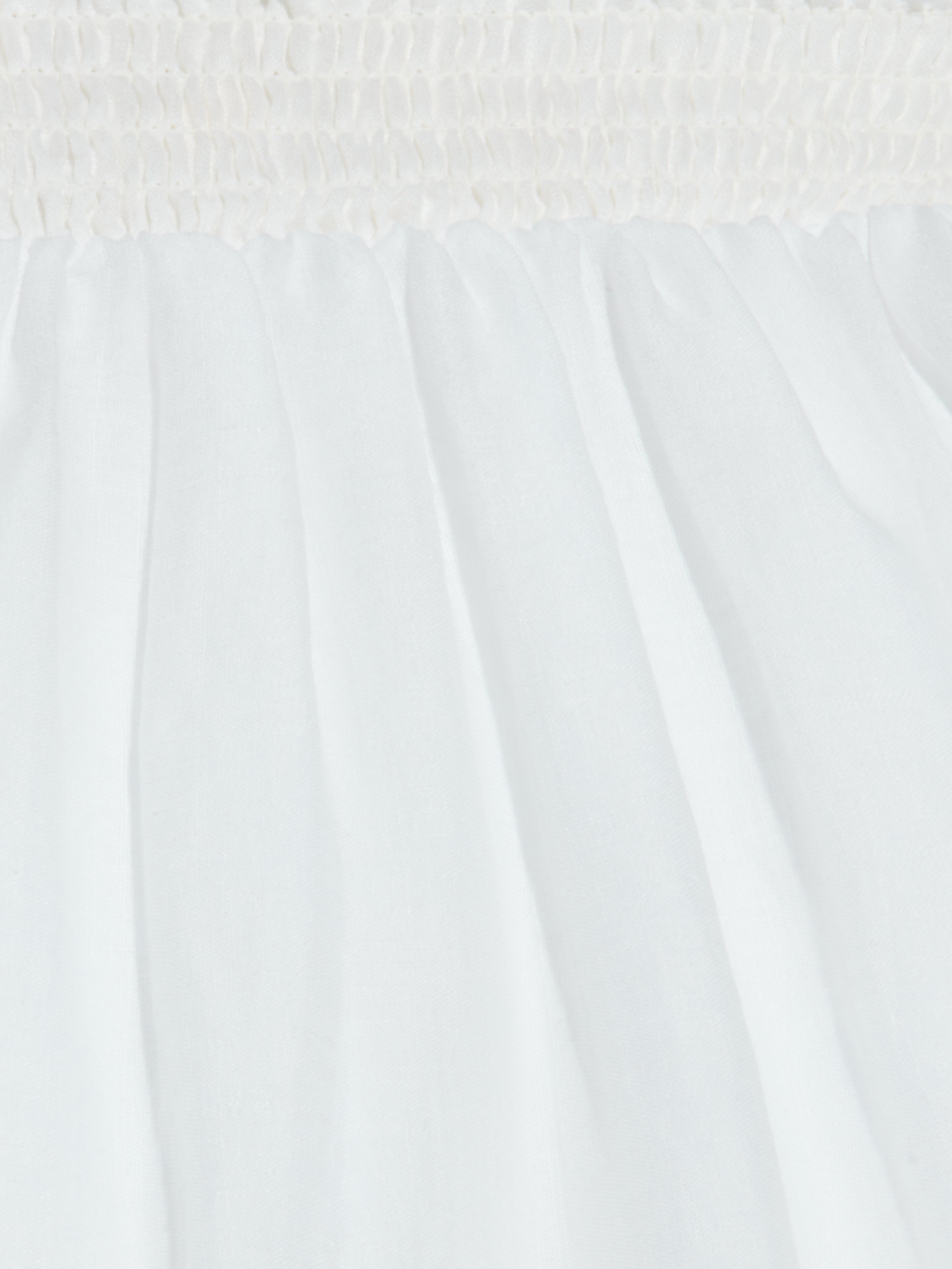 Close-up of white fabric with a ruched, gathered elastic waistband at the top and soft pleats flowing downward, creating a textured, airy appearance—perfect for the breathable Evangelina Maxi Skirt.