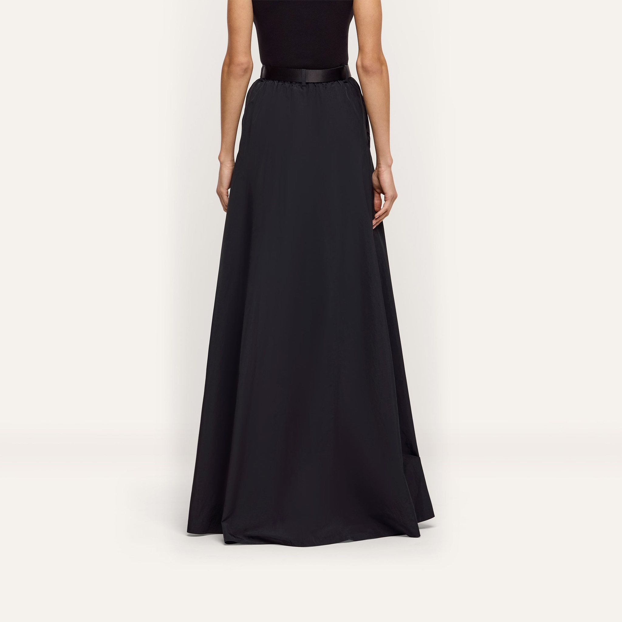 Back view of a person wearing a floor-length black water-repellant Sylas Nylon Skirt with a solid waistband.