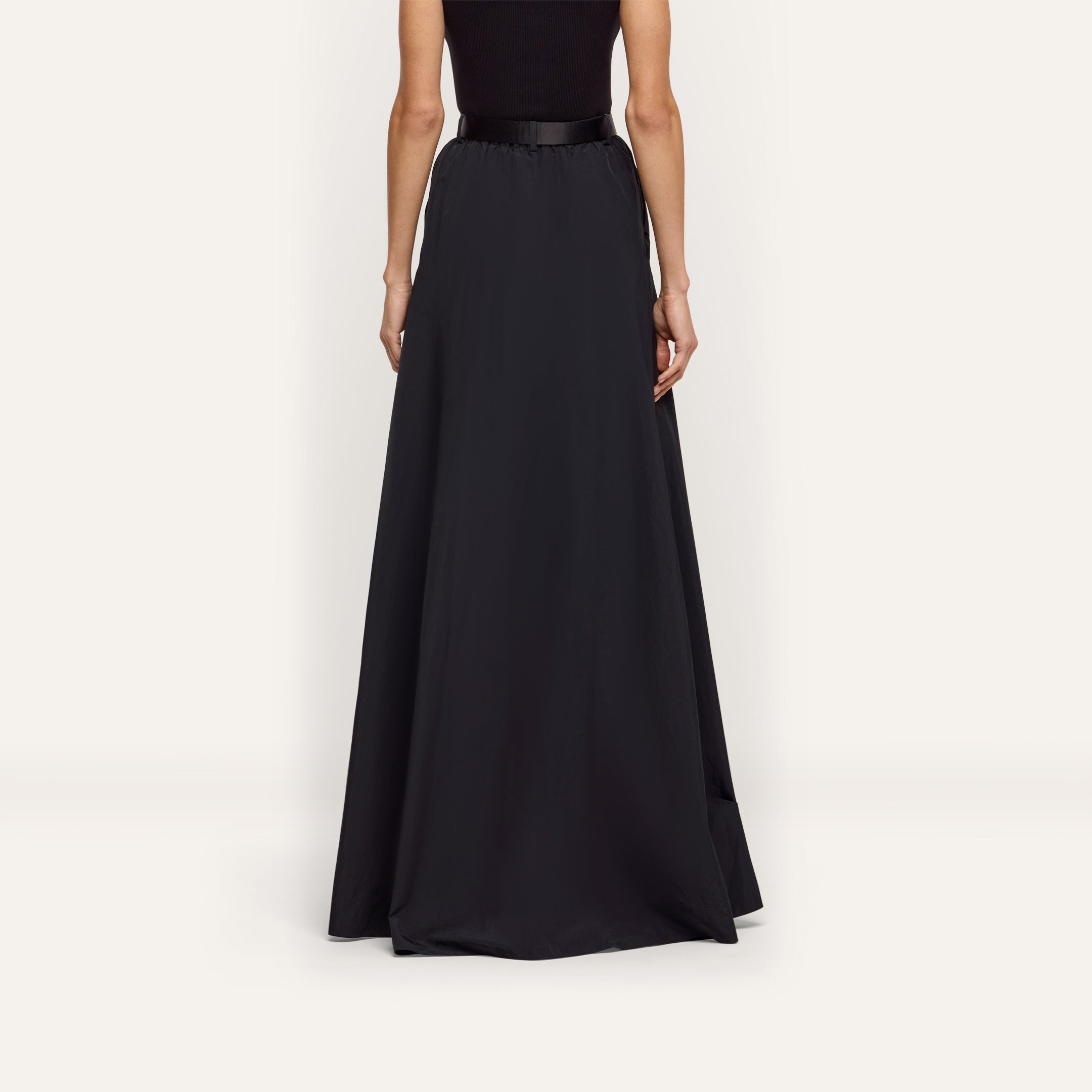 Back view of a person wearing a floor-length black water-repellant Sylas Nylon Skirt with a solid waistband.