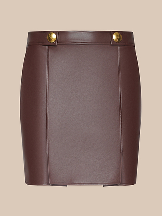 The Nolina Mini Skirt, crafted from mahogany brown vegan leather, features vertical seam details and two gold buttons at the waist, and is displayed on a plain beige background.