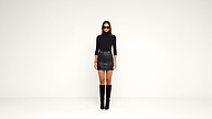 A woman in a black turtleneck, black leather mini skirt, tall black boots, and sunglasses stands against a plain white background.