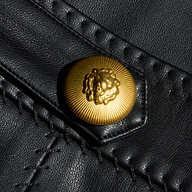 Close-up of a gold lion’s head embossed button on black Arlena Vegan Leather Mini Skirt, featuring visible whip-stitch seams and detailed stitching.