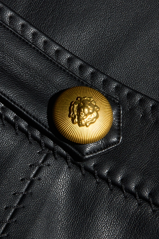 Close-up of a gold lion’s head embossed button on black Arlena Vegan Leather Mini Skirt, featuring visible whip-stitch seams and detailed stitching.