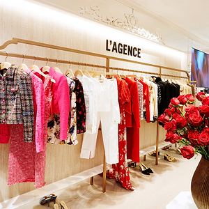 Fashion store interior with 'L'AGENCE' branding, clothing racks, and a vase of red roses.