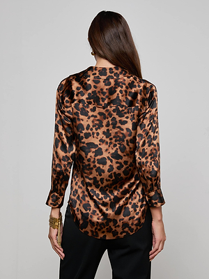 A person with long brown hair, seen from behind, wears the Dani Silk Blouse by L'AGENCE in a leopard print and black pants, standing against a plain light gray background.