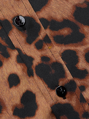 Close-up of the L'AGENCE Dani Silk Blouse, featuring a brown leopard print with black spots and two black buttons along a stitched seam.