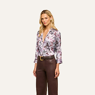 A woman with long blonde hair is wearing the Dani Silk Blouse—a button-down top featuring a mauve butterfly print—paired with high-waisted brown leather pants, standing against a plain light background.