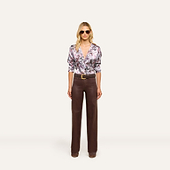 A woman wearing sunglasses, a mauve butterfly print Dani Silk Blouse, wide-leg brown trousers, and brown shoes stands facing forward against a plain white background.