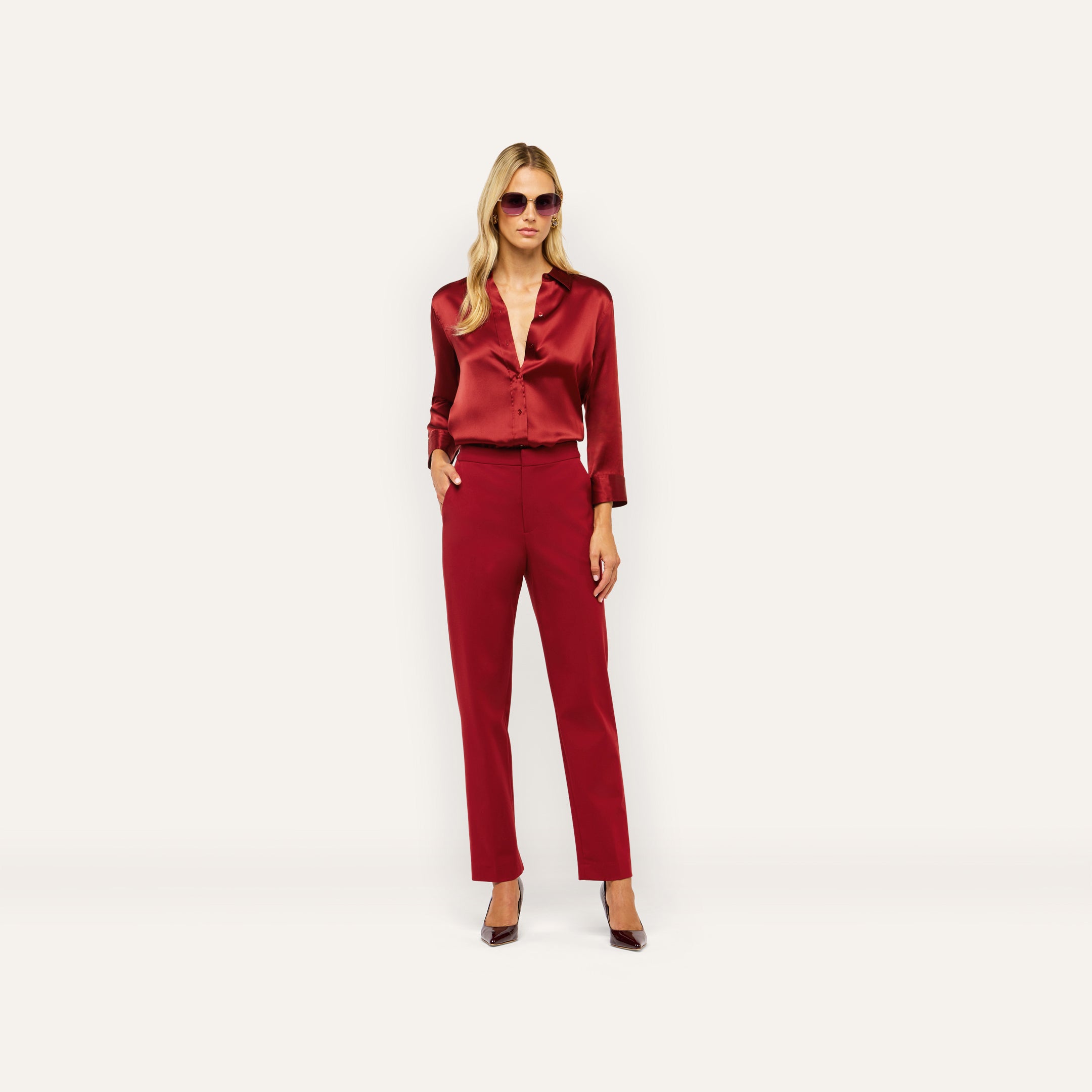 A woman wearing a dark red silk Dani Silk Blouse, matching trousers, and dark sunglasses.