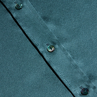 Close-up of a cadet blue Dani Silk Blouse featuring a diagonal row of iridescent buttons. The smooth, slightly shiny silk fabric showcases subtle highlights and shadows across its surface.