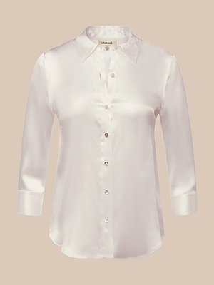 The Dani Silk Blouse is a white, long-sleeve button-down with a collar, shown on a beige background. Made from silk charmeuse, it features a sleek shiny finish, slim fit silhouette, and six front buttons.