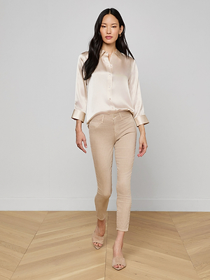A woman in the Dani Silk Blouse in champagne, paired with beige fitted pants and nude heels, walks confidently on a light wood floor against a plain light gray wall.