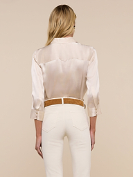 A woman with long blonde hair stands with her back to the camera, wearing the cream-colored Dani Silk Blouse paired with matching pants against a plain light background.