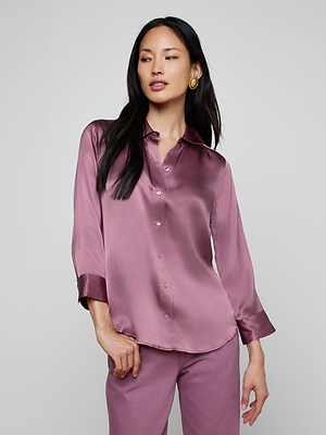 A woman with long dark hair poses confidently against a plain light gray background, wearing the shiny mauve Dani Silk Blouse and matching pants.