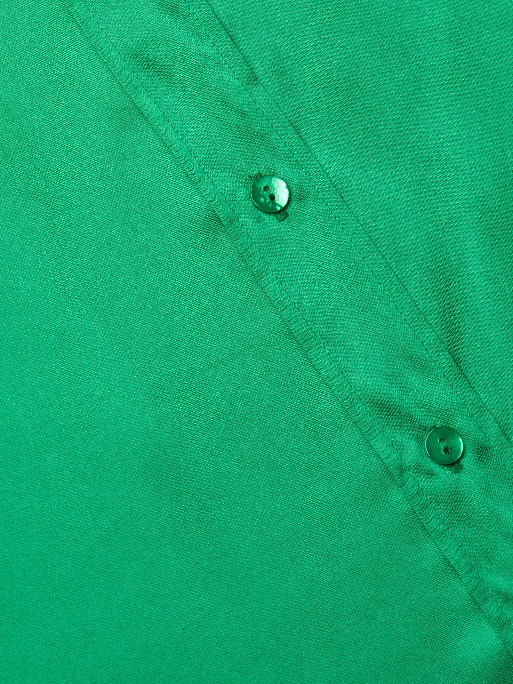 Close-up of a green Dani Silk Blouse highlighting two buttons and part of a seam, with smooth silk button-down fabric texture.
