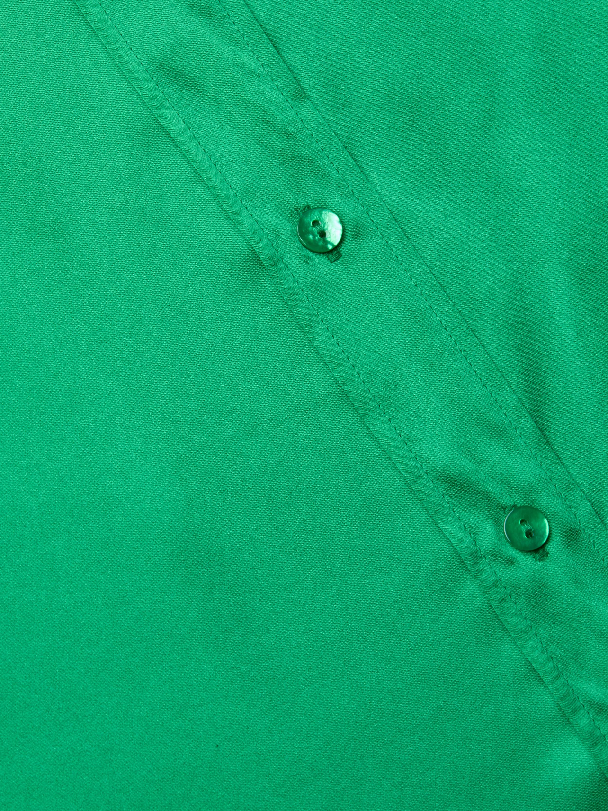 Close-up of a green Dani Silk Blouse highlighting two buttons and part of a seam, with smooth silk button-down fabric texture.