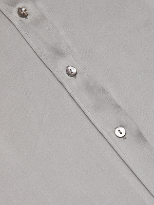 Close-up of a light gray Dani Silk Blouse fabric featuring a diagonal row of silver buttons along the seam.