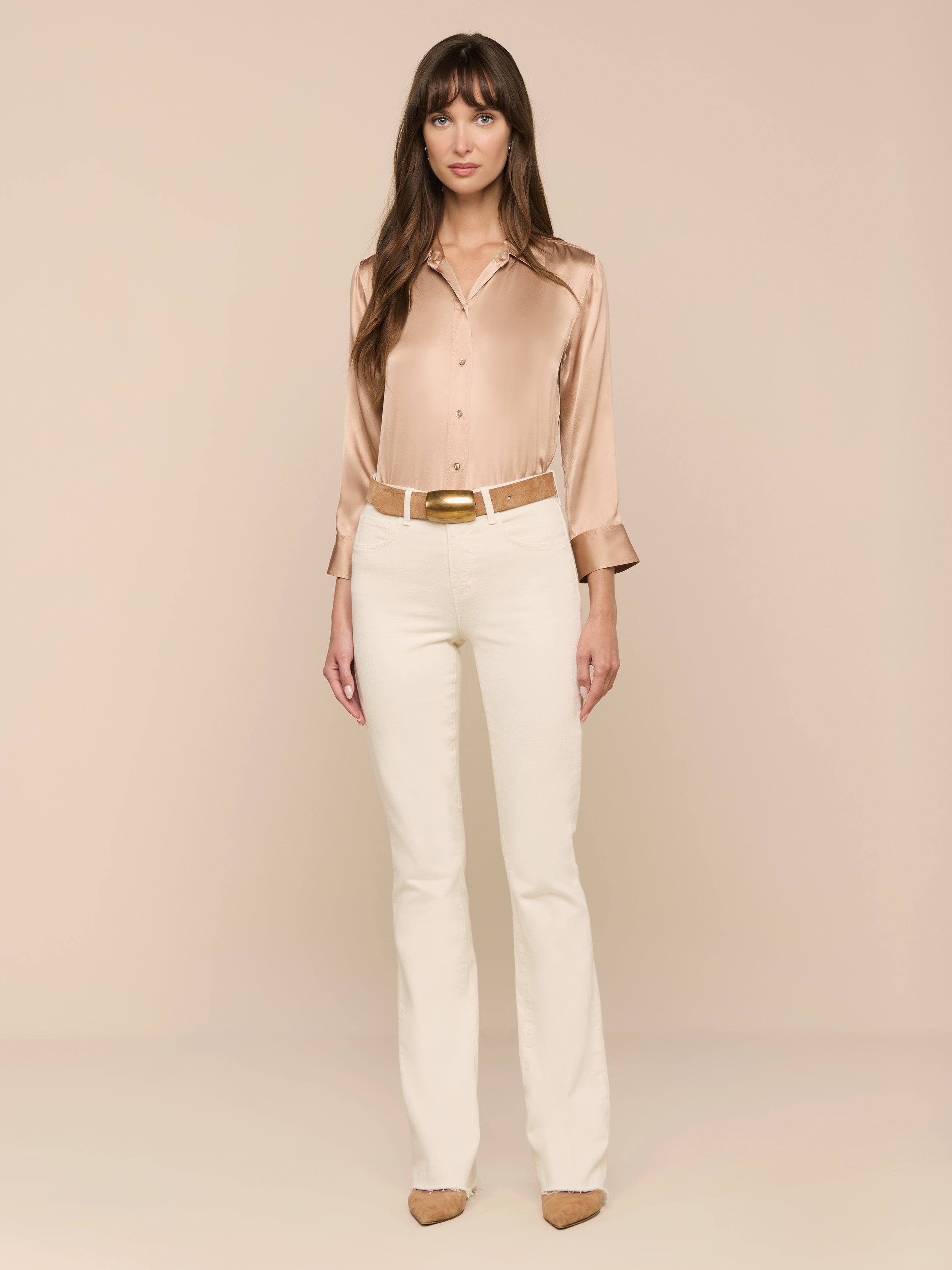 A woman stands facing forward against a plain white background, wearing the Dani Silk Blouse in beige with three-quarter sleeves, paired with cream-colored pants and tan heels.