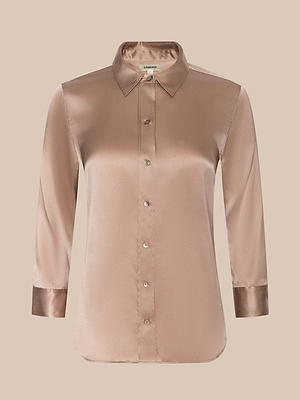 The Dani Silk Blouse is a womens satin silk button-down in champagne with a pointed collar and shiny cuffs. This long-sleeve blouse is shown against a beige background.