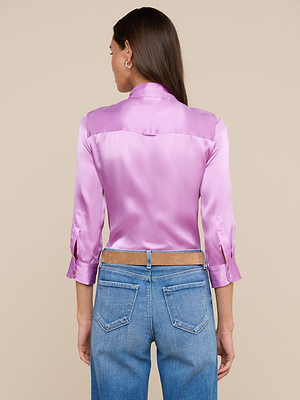 A woman with long brown hair is seen from the back in a shiny pink Dani Silk Blouse with three-quarter sleeves and blue jeans, set against a beige background.