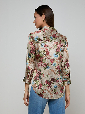 A woman with straight brown hair wears a long-sleeved Dani Silk Blouse in a floral tapestry print and blue jeans. She faces away from the camera, showing the back of her blouse against a plain light background.