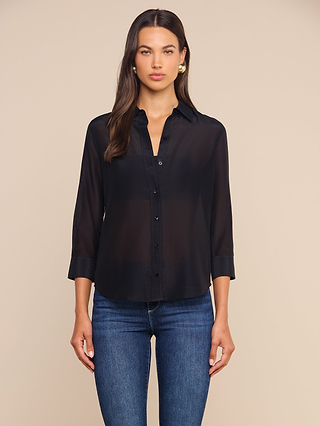 A woman stands against a plain beige background wearing the Dani Cotton-Silk Blouse in black, featuring three-quarter sleeves, paired with blue jeans.