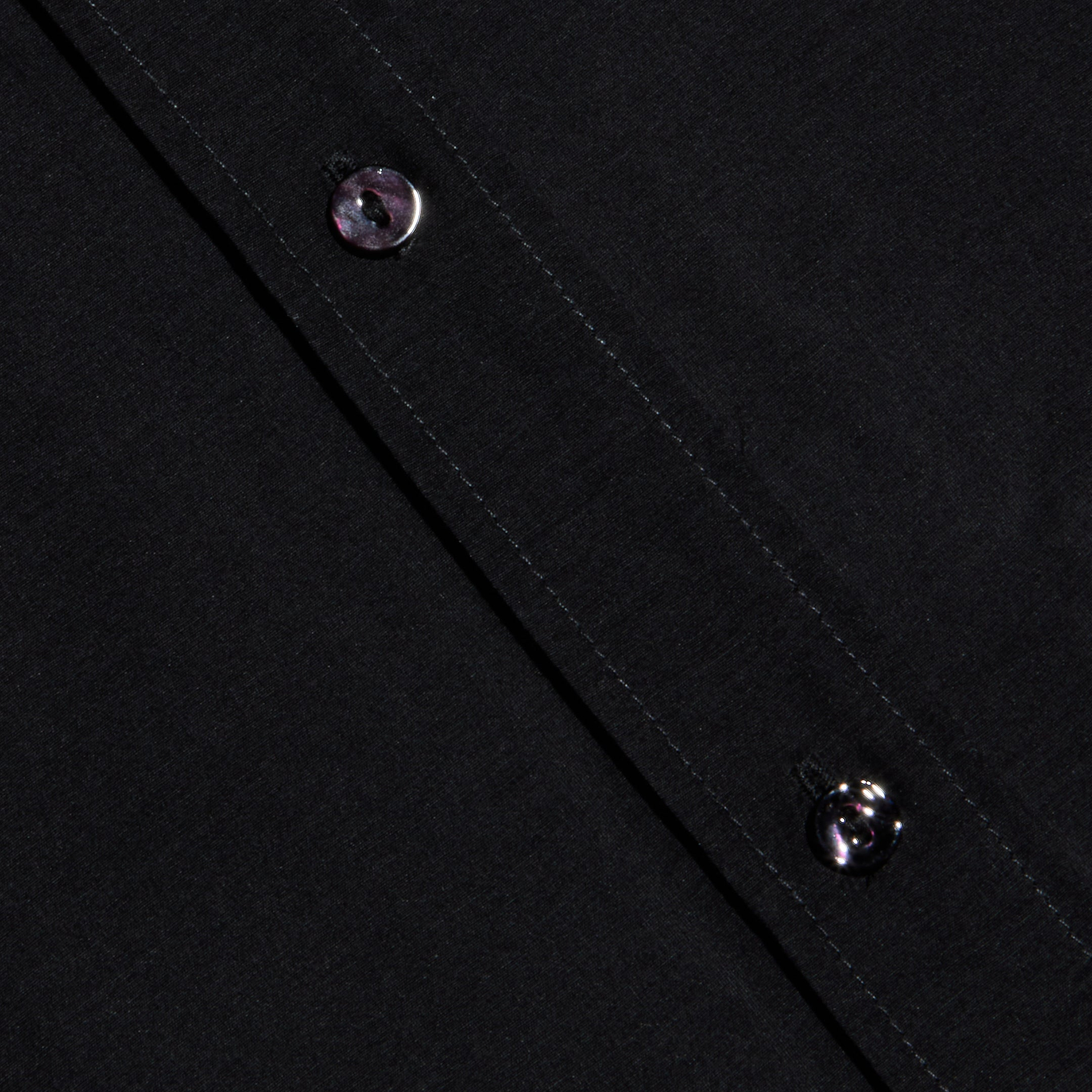 Close-up of the Dani Cotton-Silk Blouse fabric in black, featuring two black buttons along a diagonal seam with visible stitching.