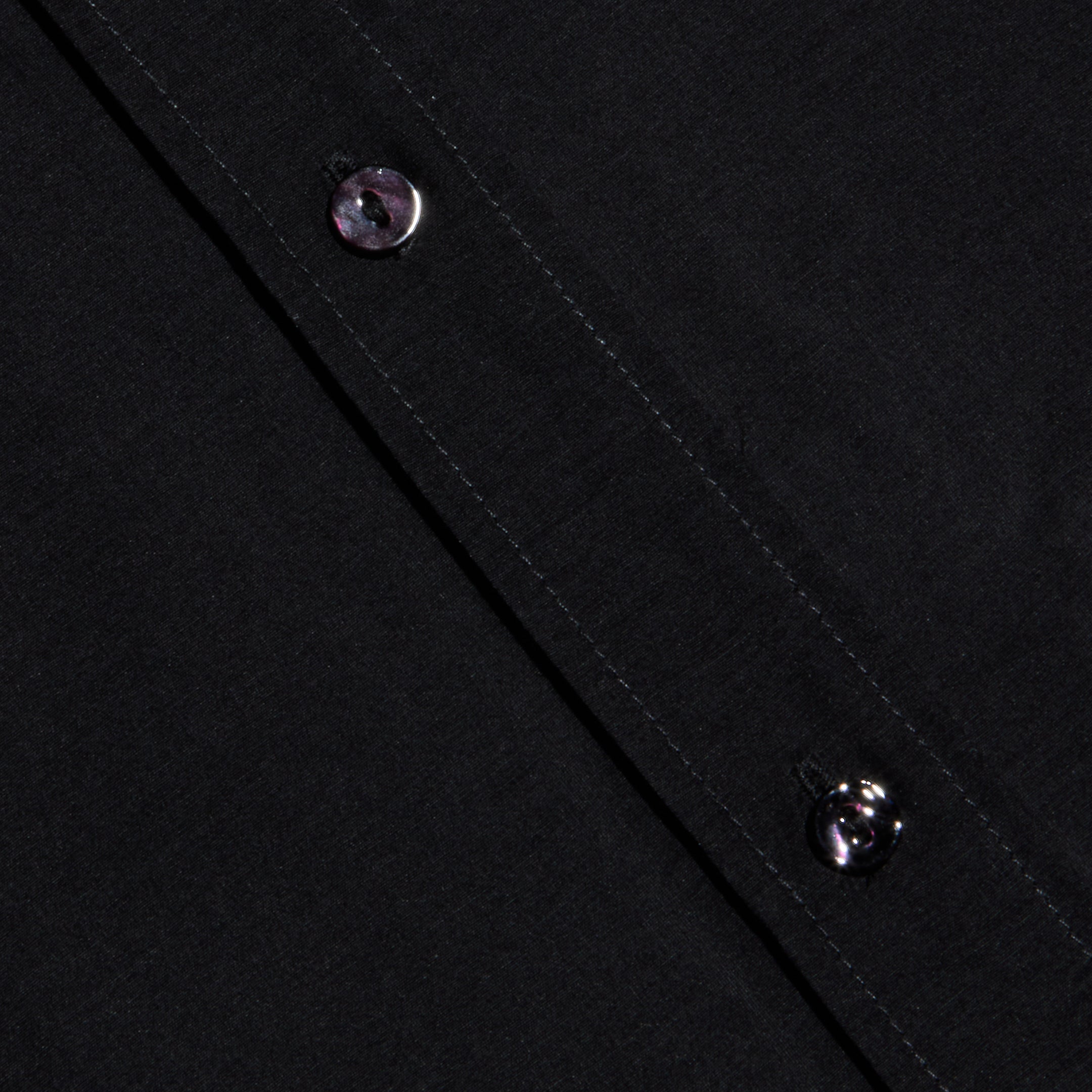 Close-up of the Dani Cotton-Silk Blouse fabric in black, featuring two black buttons along a diagonal seam with visible stitching.