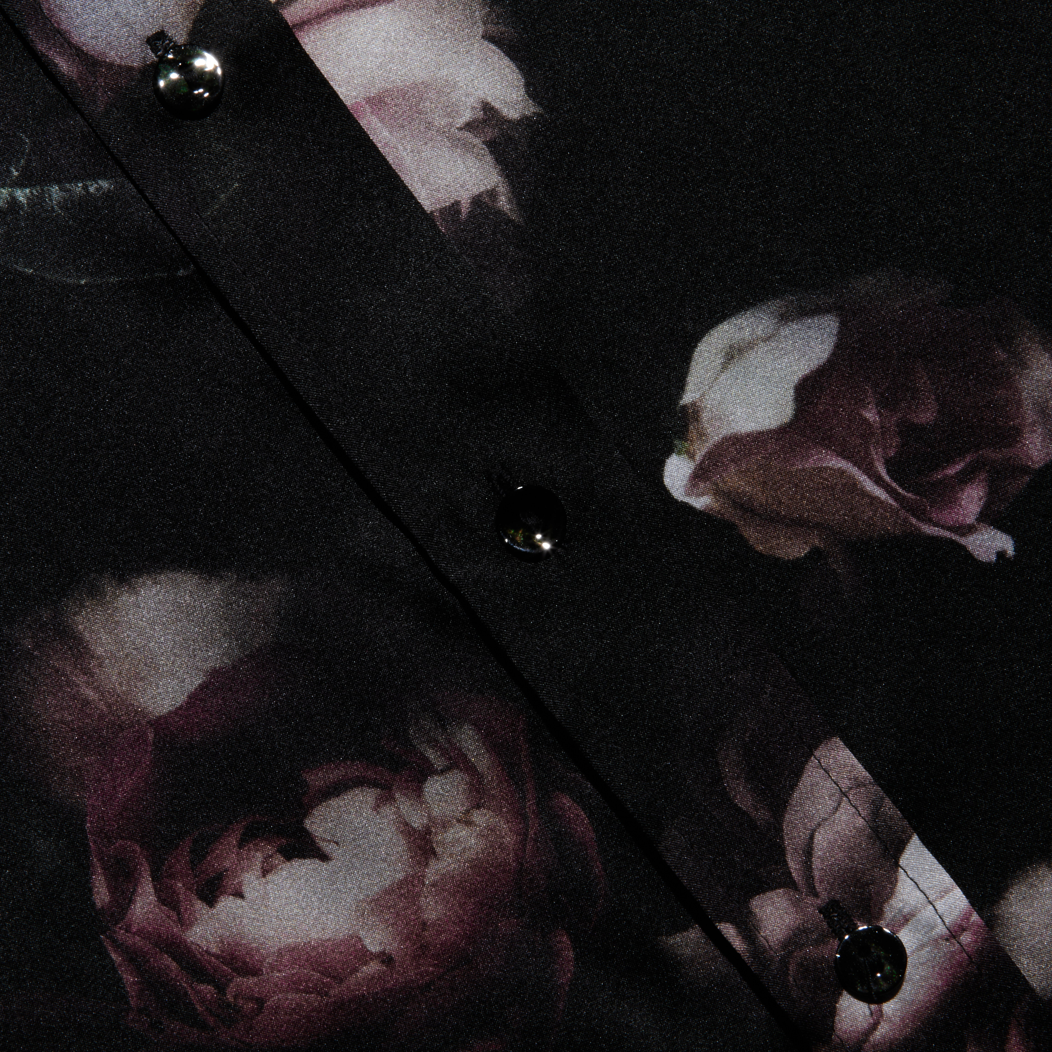 Close-up of the Dani Silk Blouse in silk charmeuse, styled in a dark hue with shiny black buttons and a floral pattern of pink and white roses.