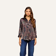 A woman wearing the Dani Silk Blouse, a long-sleeve, button-down shirt in a dark paisley print, paired with blue jeans and standing against a plain light background.