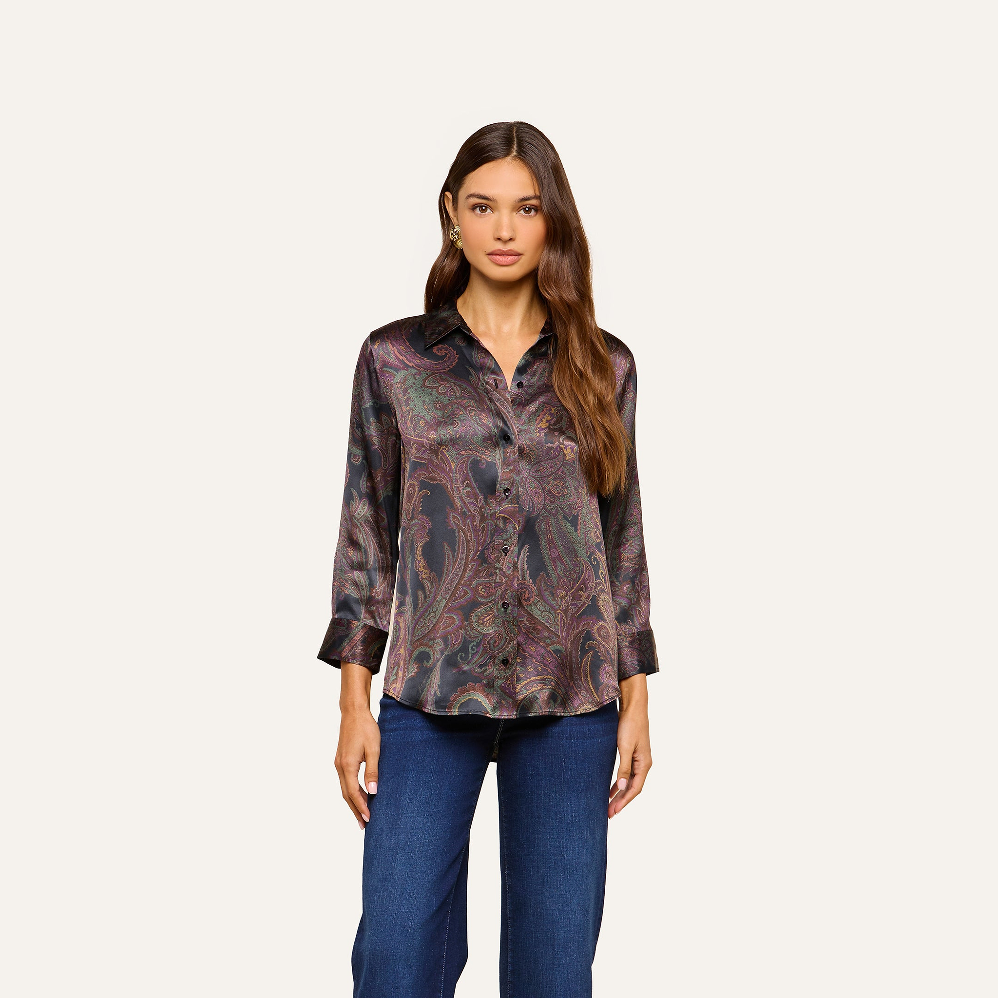 A woman wearing the Dani Silk Blouse, a long-sleeve, button-down shirt in a dark paisley print, paired with blue jeans and standing against a plain light background.