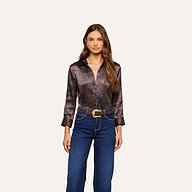 Woman with long brown hair wears the Dani Silk Blouse—a dark paisley shirt with three-quarter sleeves—paired with blue jeans and a decorative belt, standing against a plain off-white background.